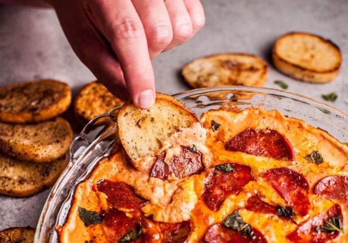 hand dipping garlic bread into chorizo pizza dip