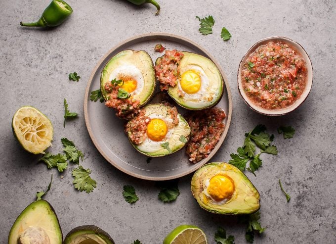 four huevos rancheros avocados on a plate next to dish of homemade salsa