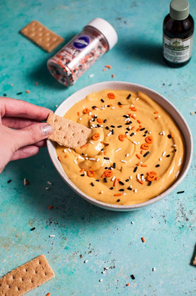 a hand dipping a graham cracker into homemade pumpkin cheesecake dip