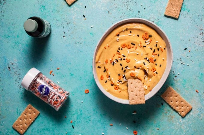 bowl of pumpkin cheesecake Halloween dip next to jar of orange and black sprinkles