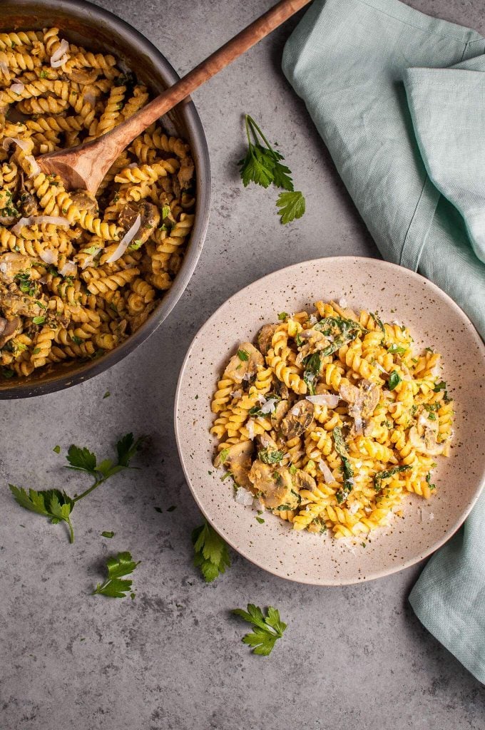 skillet with wooden spoon and bowl of pumpkin, mushroom, and spinach pasta