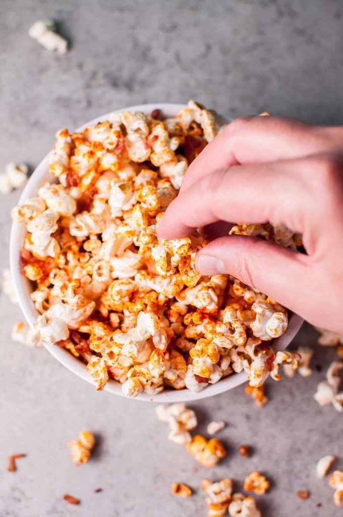 hand reaching into bowl of popcorn with sriracha and bacon seasoning