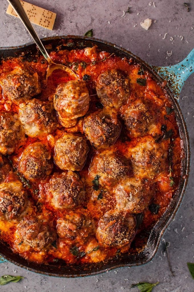 close-up of meatballs in a rich tomato sauce with melted cheese in a skillet