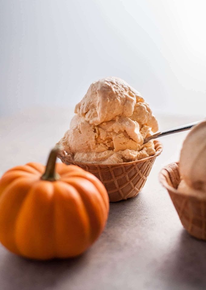 ice cream cone cup with scoop of homemade cinnamon pumpkin ice cream with a small pumpkin in the foreground