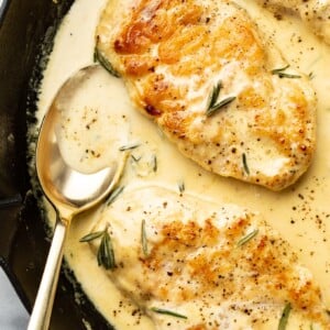 closeup of rosemary dijon chicken in a skillet with a serving spoon