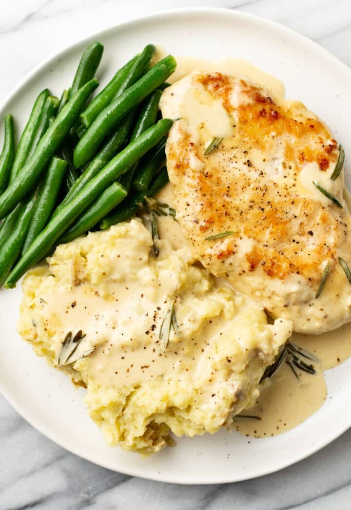 a plate with chicken in sauce, green beans, and mashed potatoes