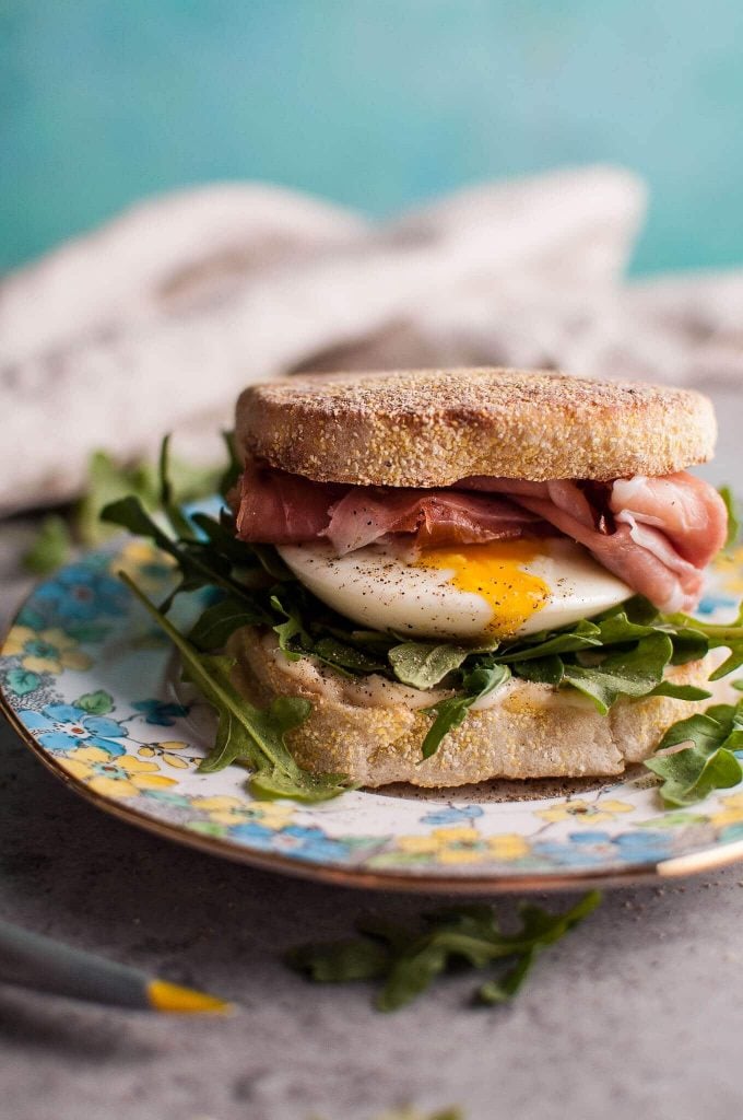 close-up of poached egg and prosciutto brunch sandwich on a flower plate