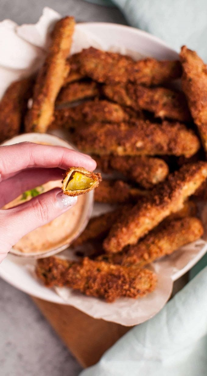 a hand holding a crispy battered fried pickle