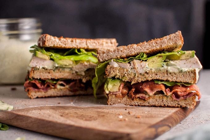 homemade green goddess chicken sandwich with bacon and avocado cut in half on a cutting board