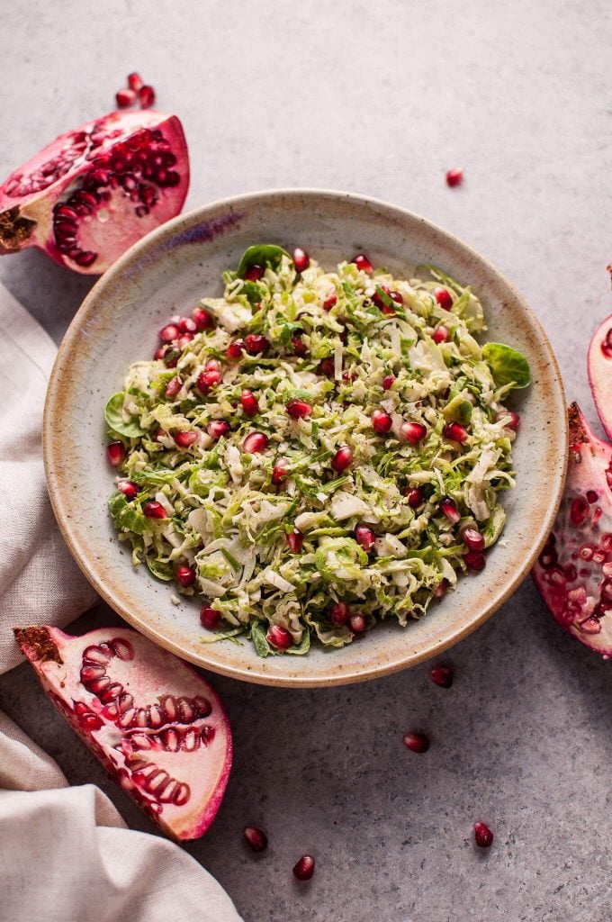 pomegranate Brussels sprouts fall salad in a bowl next to sliced pomegranates