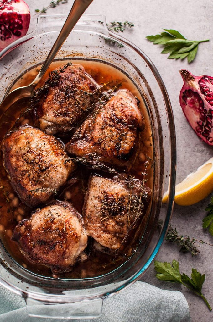 pomegranate lemon roasted chicken in a glass dish with a serving spoon