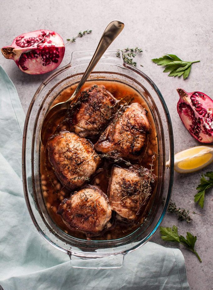 glass baking dish with pomegranate lemon roasted chicken with herbs and serving spoon