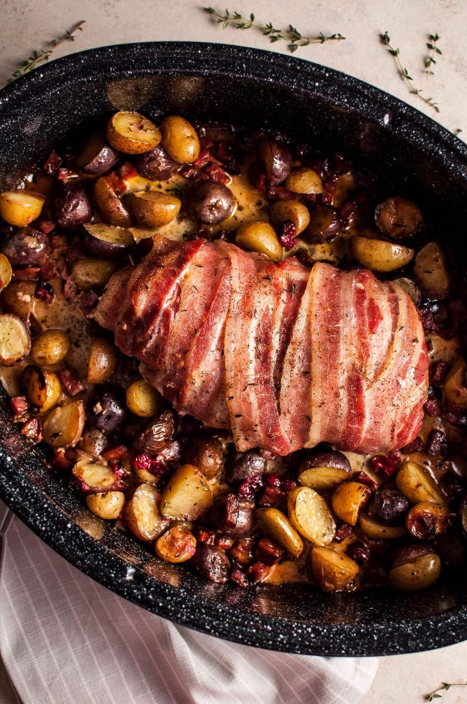 close-up of bacon-wrapped turkey breast with chorizo, cranberries, and potatoes in a roasting pan