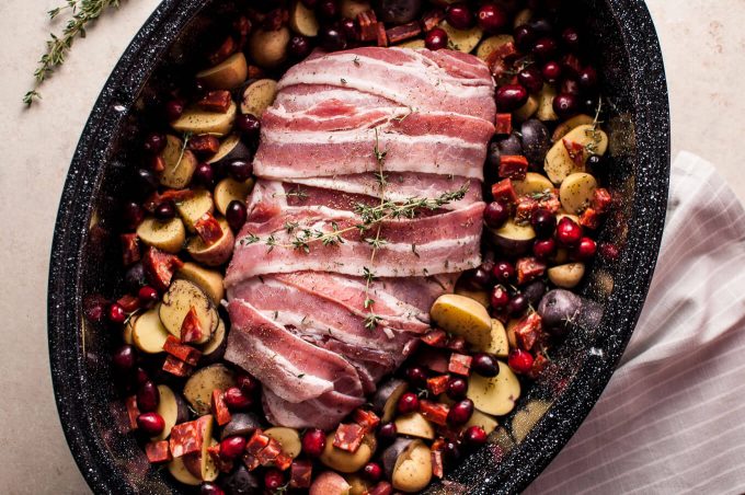 bacon wrapped turkey breast with chorizo, cranberries, and little potatoes in a baking dish ready for the oven