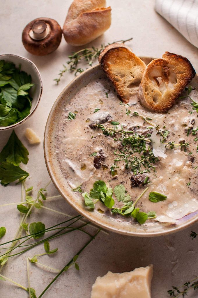 bowl of loaded creamy mushroom soup with toasted garlic baguette slices, truffle oil, and parmesan toppings