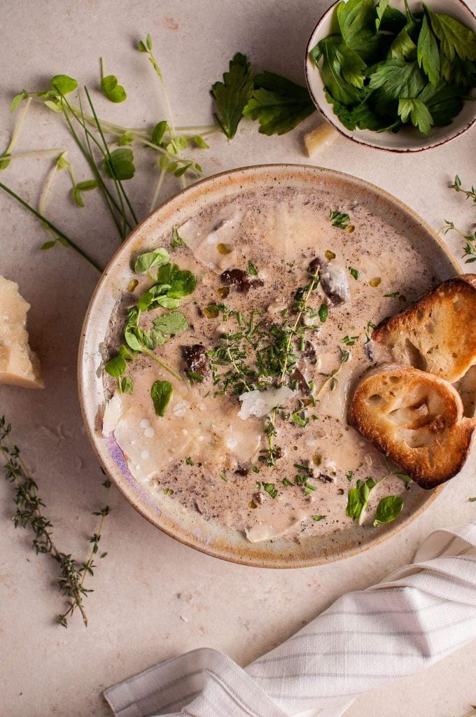 bowl of creamy mushroom soup with toasted baguette slices and herb garnish