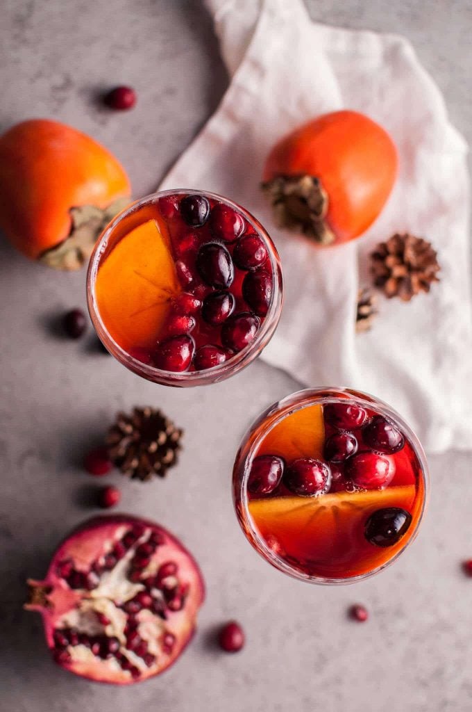 two glasses of pomegranate and persimmon winter sangria next to two whole persimmons