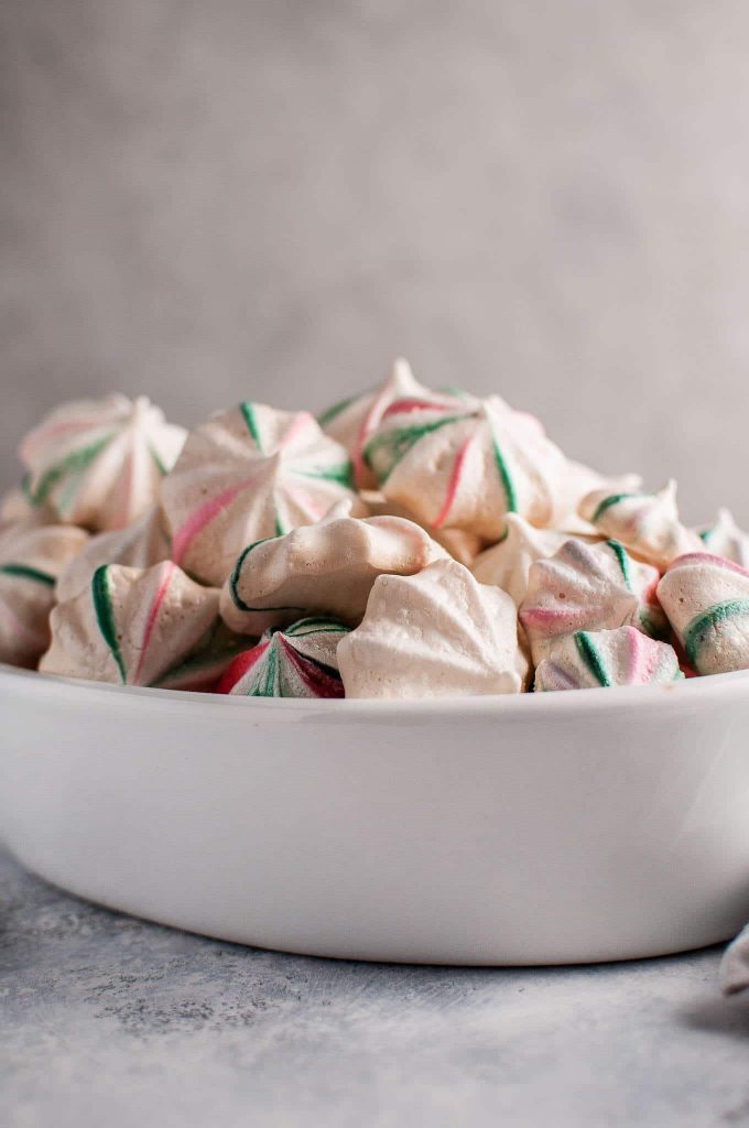 white bowl with several red and green holiday meringue cookies