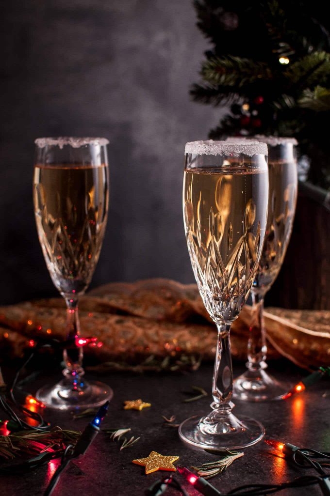 three glasses of pear champagne cocktail beside Christmas lights and tree