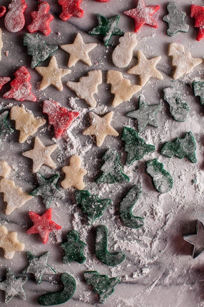 several homemade red and green marzipan Christmas treats in festive shapes with powdered sugar beside star shaped cookie cutter