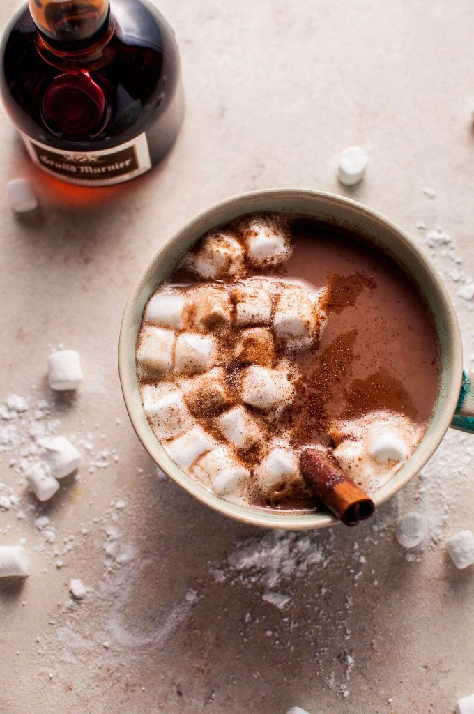 close-up of a mug of orange spiked boozy hot chocolate with marshmallows and a cinnamon stick