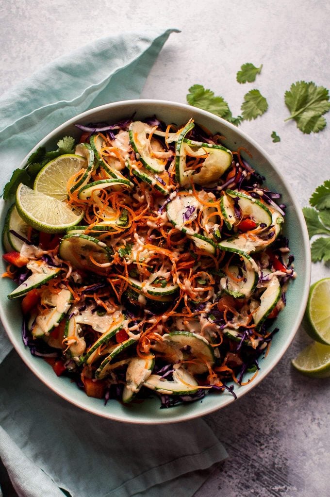 bowl of healthy spiralized Thai salad with cilantro lime peanut dressing with lime wedges and cilantro sprigs