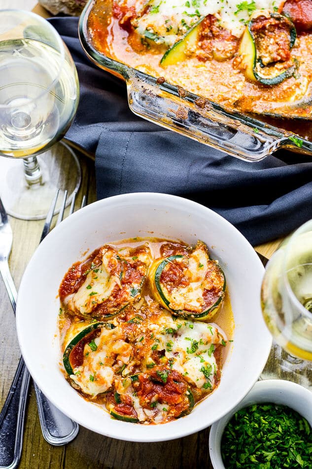 bolognese zucchini lasagna roll-ups in a bowl beside glass of white wine