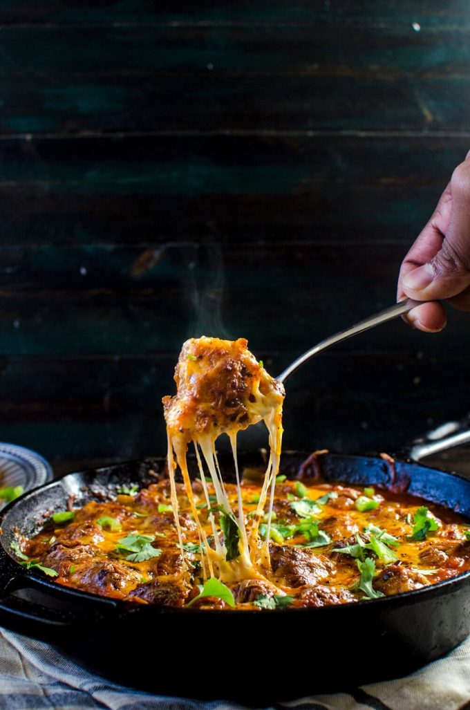 cheesy Mexican meatball skillet with a hand holding a fork