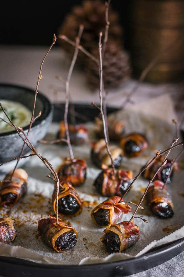 several bacon-wrapped prunes on a plate beside herb dip