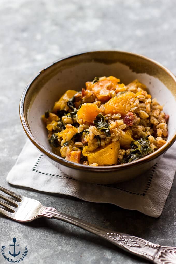 a bowl of baked farro with butternut sqaush, pancetta, and kale and a fork