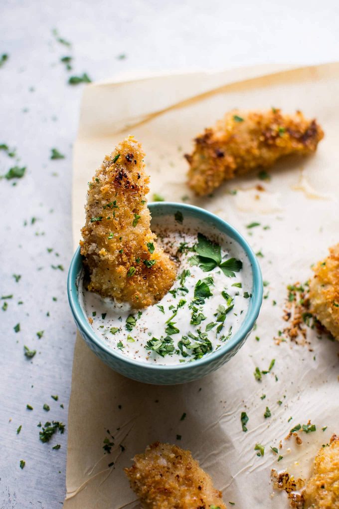 baked sticky lemon chicken tenders on parchment paper with a small bowl of homemade ranch dipping sauce