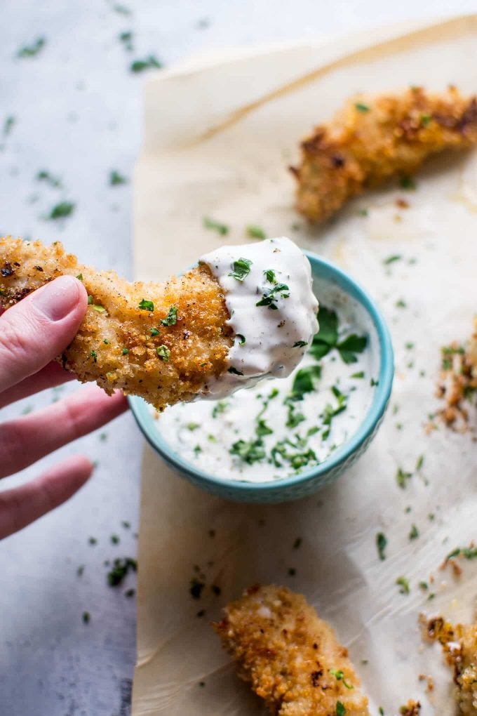 hand holding a baked lemon chicken tender dipped in homemade ranch dip