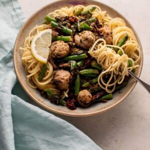 healthy chicken sausage pasta in a beige bowl with spaghetti twirled on a fork