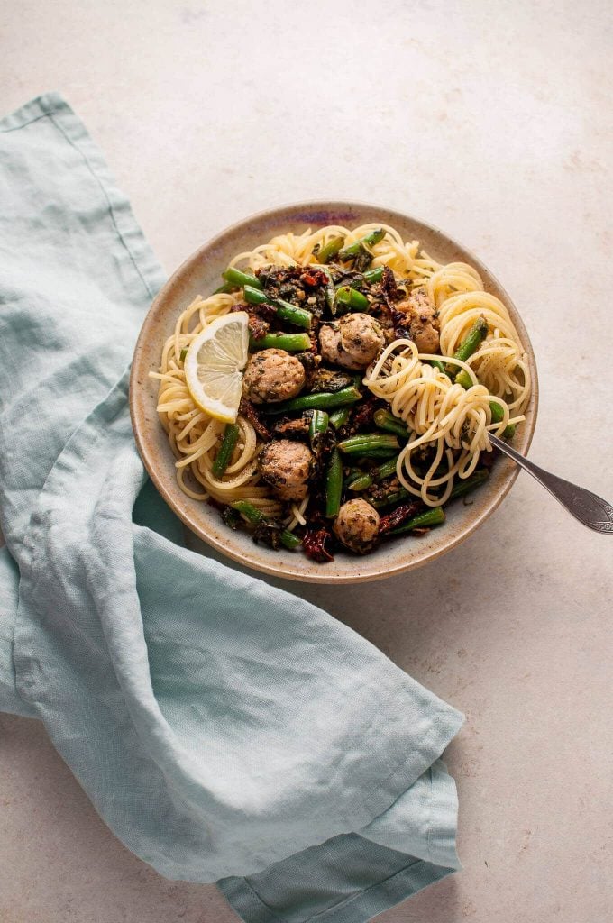 bowl of healthy chicken sausage pasta with a fork next to a cloth napkin