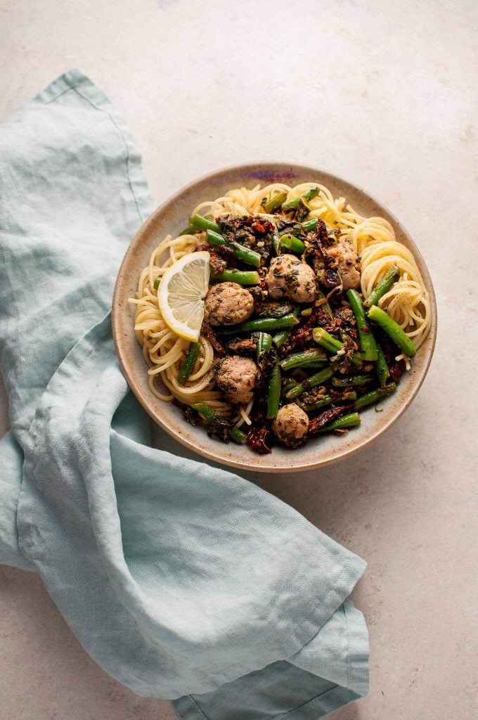 bowl of chicken sausage pasta with green beans and a slice of lemon