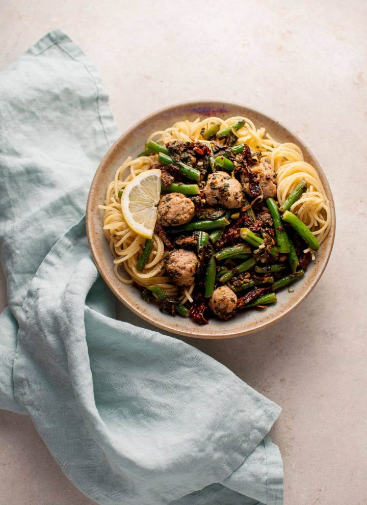 bowl of healthy chicken, sausage, and green beans pasta next to a cloth napkin