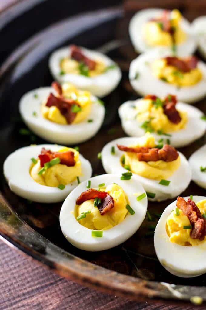 several deviled eggs in halves with bacon and chives on a plate