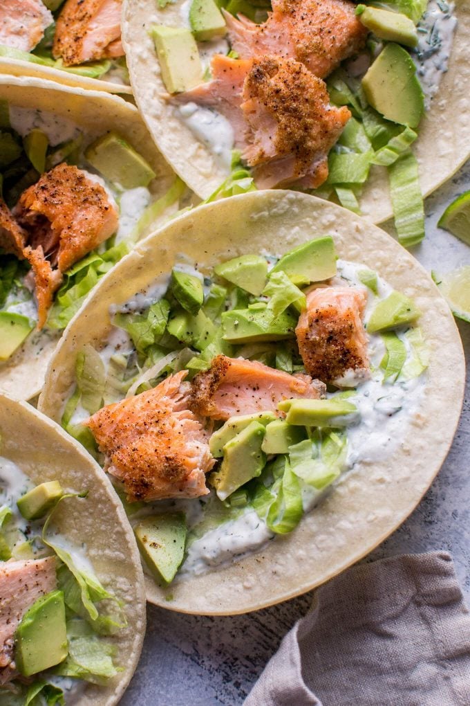 close-up of several healthy baked salmon tacos with avocado and cilantro lime yogurt dressing