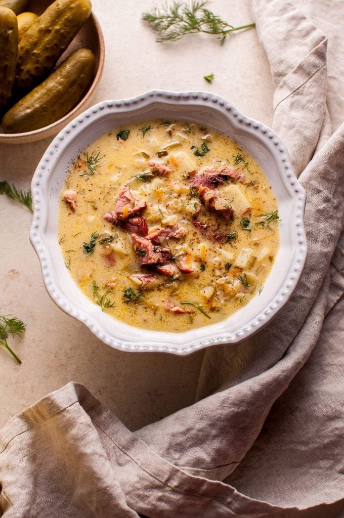 white bowl with Polish dill pickle soup with smoked ham beside a cloth napkin