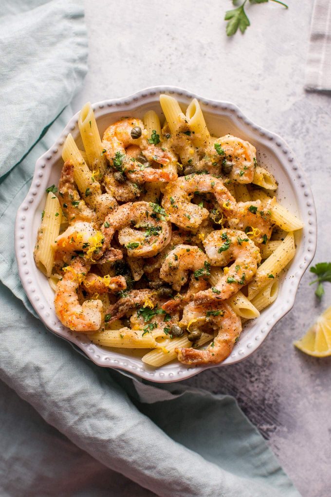 white bowl with easy shrimp piccata served over penne beside cloth napkin and lemon slice