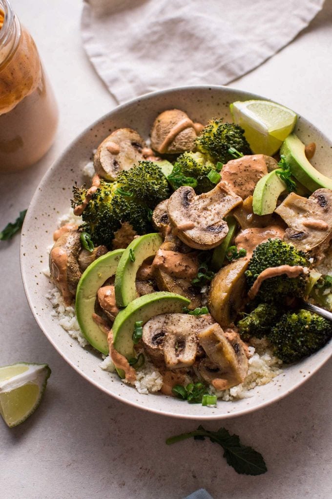 vegetarian Buddha bowl with mushrooms, avocado, and broccoli on cauliflower rice next to jar of dressing
