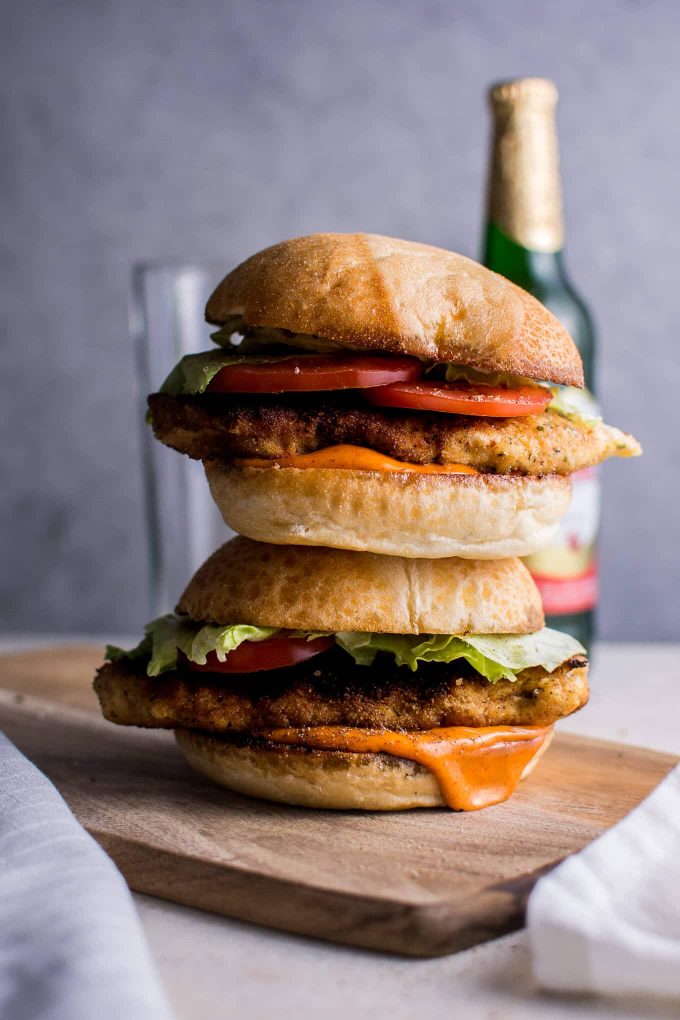 two spicy breaded fried chicken sandwiches on a table with a bottle of beer and a glass