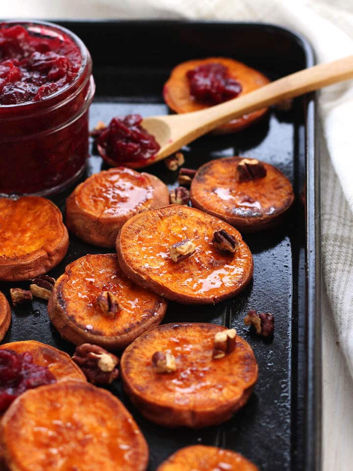several roasted sweet potato rounds on a sheet pan with a wooden serving spoon