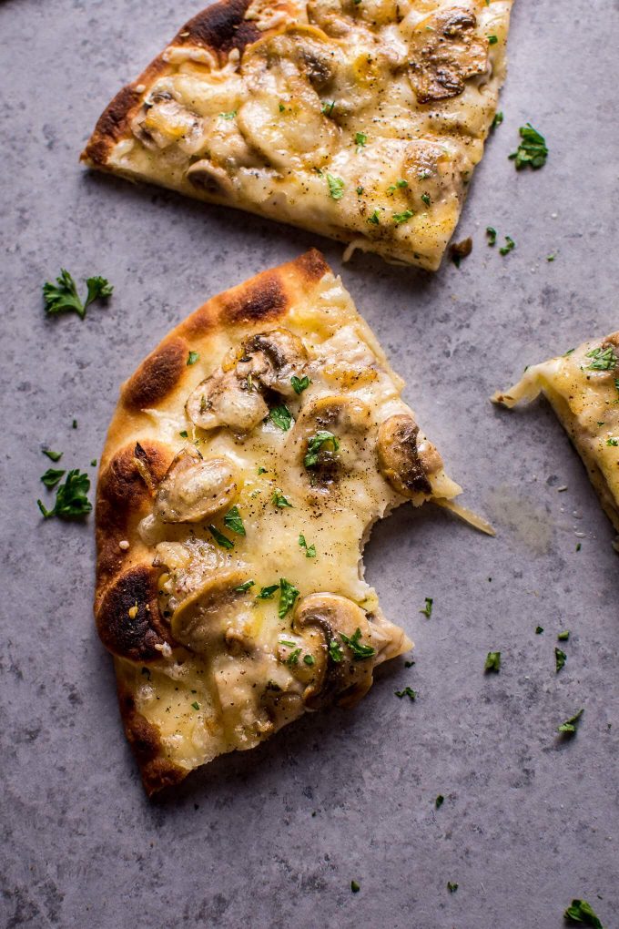 A slice with a bite taken of vegetarian naan pizza with Fontina cheese and mushrooms