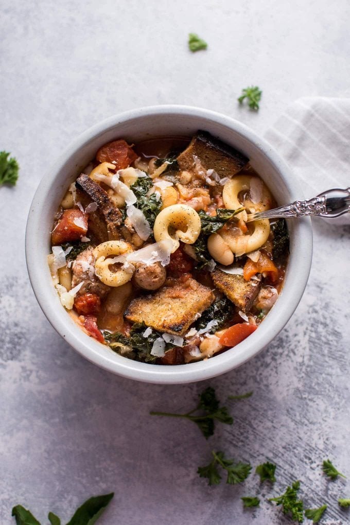 tuscan chicken soup with white beans, kale, and pasta in a white bowl with a spoon