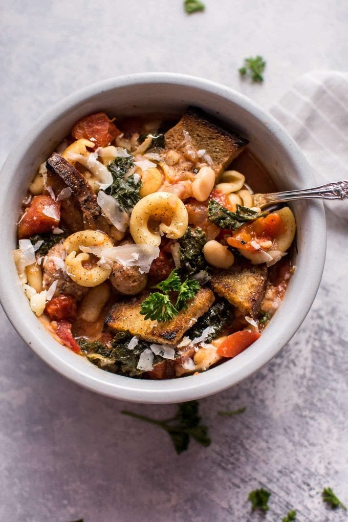 tuscan chicken soup with white beans, kale, and pasta in a white bowl with a spoon close-up