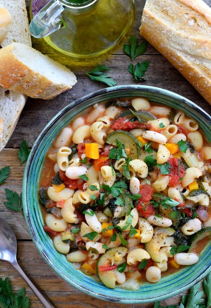 a bowl of vegetarian pasta fagioli on wooden surface with slices of bread