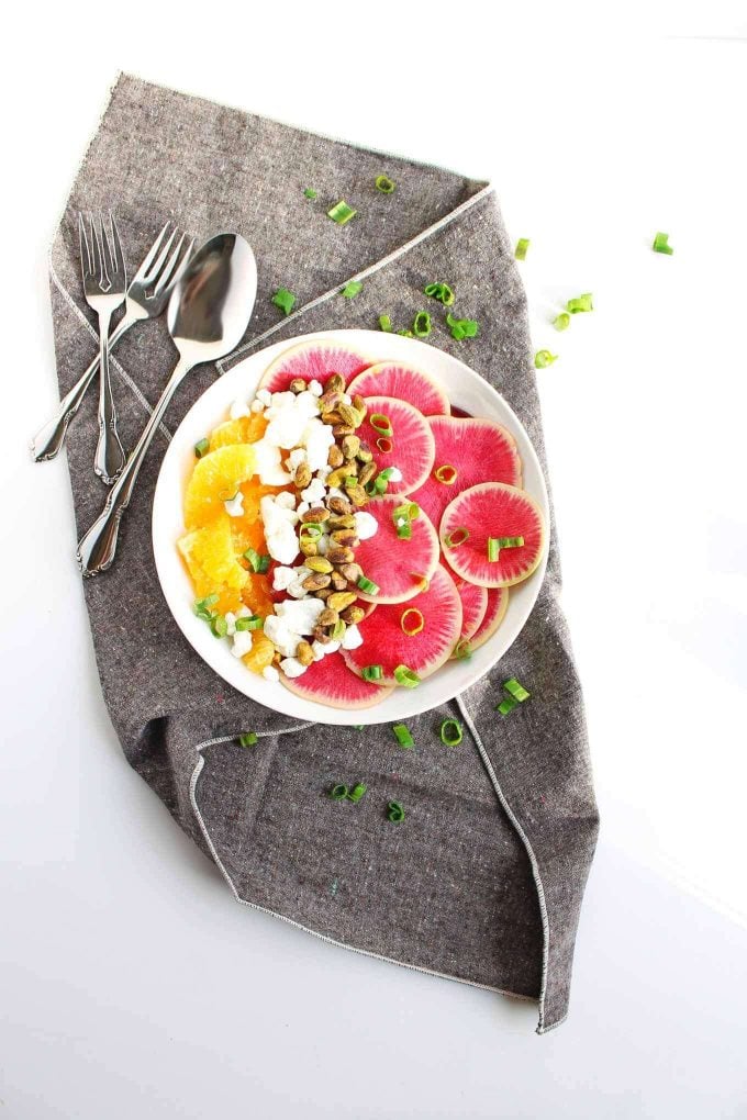 watermelon, radish, and orange salad on a plate beside forks and spoon