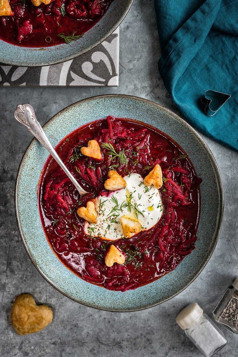 bowl of beet borscht with tiny puff pastry hearts and a spoon