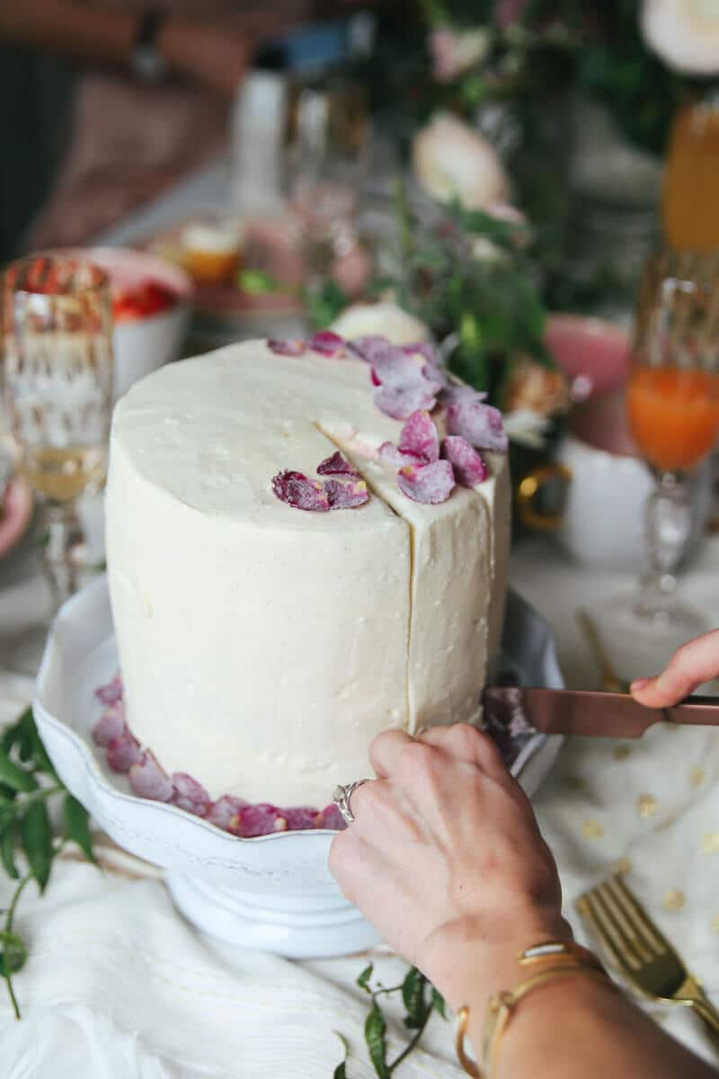 hands slicing a whole cake with candied flower petals on top of icing